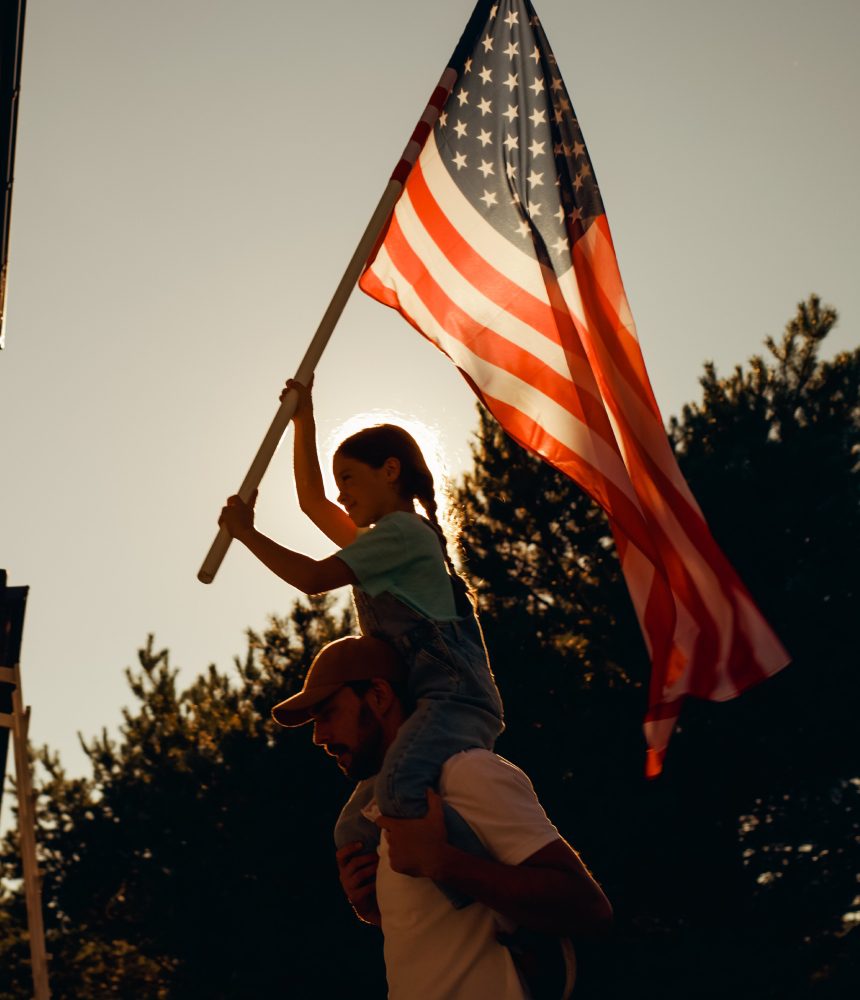 Girl on dad's shoulders, waving American flag.